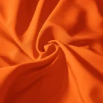 Close up of bright orange fabric with soft folds and a central knot or twist in the center of the image | PricZone