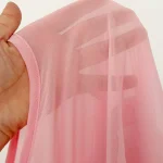 Close up of a pale pink sheer scarf held by a hand showing a stitched edge and subtle stripes in the fabric | PricZone