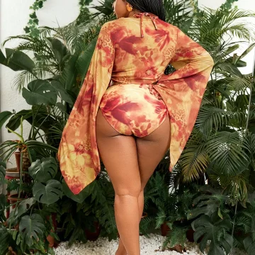 Woman standing with her back to the camera in a orange red tie dye cover up revealing a high cut swimsuit bottom among tropical plants | PricZone