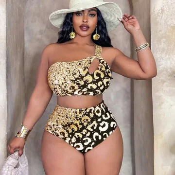 Woman in a gold leopard-print bikini with a wide-brim straw hat, posing in a stone doorway with gold jewelry.