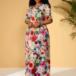 Plus Size Floral Print Maxi Dress 1 | PricZone Woman posing in a colorful floral maxi dress against a beige wall with jewelry and sandals | PricZone
