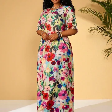 Woman posing in a colorful floral maxi dress against a beige wall, with jewelry and sandals.