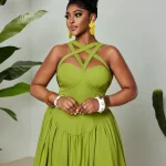 Woman in a bright lime green crisscross strap dress posing with hands near waist against a neutral backdrop and tropical plants in the background | PricZone
