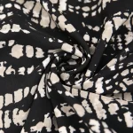 Close up of black fabric with irregular off white speckled pattern and soft foldstwist in the center | PricZone