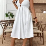 Woman in a white halter dress with a cutout standing indoors near wooden chairs and a plant | PricZone