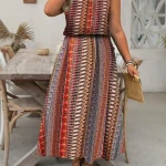 Full length view of a woman in a sleeveless brownorange tribal pattern maxi dress holding a woven straw clutch and wearing sandals | PricZone