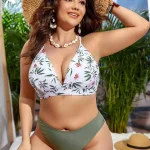 Woman in a white tropical pattern bikini top with olive bottoms wearing a large straw hat posing outdoors in sun | PricZone