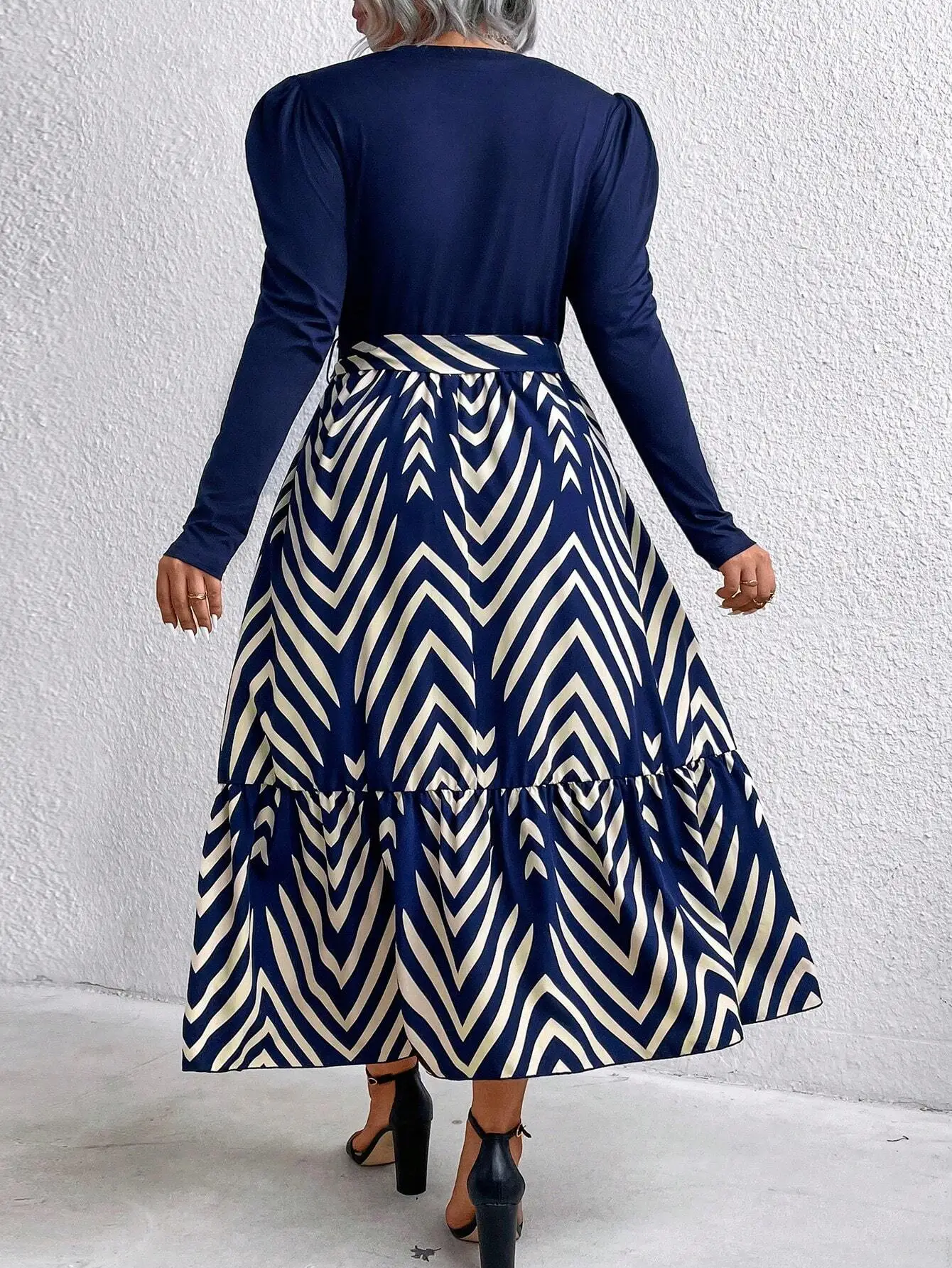 Plus Size Round Neck Long Sleeve Chevron Print Midi Dress 3 | PricZone Back view of a person wearing a navy long sleeve top and a navy and cream chevron patterned midi length skirt with a tied waistband standing against a white textured wall | PricZone