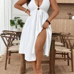 Woman in a white halter dress with a front knot and thigh high slit standing indoors by a wooden table | PricZone