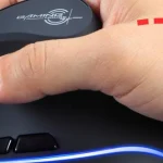 Close up of a hand gripping a black gaming mouse with blue LED lighting along the bottom edge and a logo on the top | PricZone