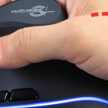 Close-up of a hand gripping a black gaming mouse with blue LED lighting along the bottom edge and a logo on the top.