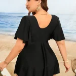 Back view of a woman in a black flutter sleeve dress standing on a beach wearing large gold circular earrings and a delicate chain necklace on a sunny day by the sea | PricZone