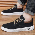 Black low top canvas sneakers with a white chunky sole tan laces and brown heel accents on a wooden floor with rolled jeans showing | PricZone
