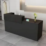 Adjustable Height Desk with Storage and Open Shelves 3995 1 | PricZone Modern black reception desk in a clean showroom with a computer monitor QR code card and a vase of white flowers on the counter clothing on a rack to the left | PricZone