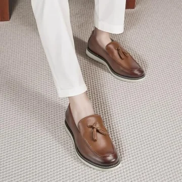 Brown leather tassel loafers worn with white pants, shown from a top-down angle on a beige carpeted floor