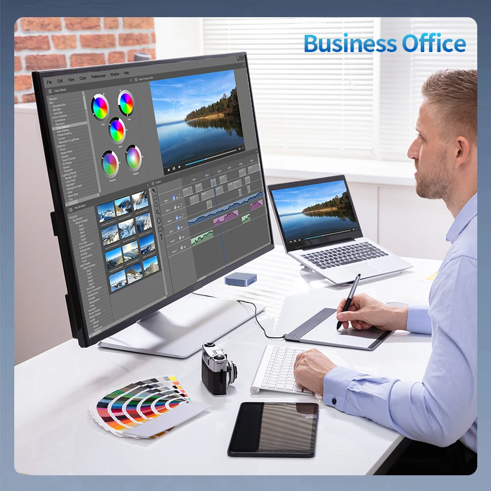 Professional video editing workspace with a man using a stylus on a graphics tablet, large monitor showing editing software and color wheels, laptop, and color swatches on a white desk. Contains the label 'Business Office' in the corner.