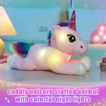 Soft pink unicorn plush with a rainbow mane and glittery pink horn resting on a pastel surface with colorful night lights in the background text on image reads cuddly unicorn stuffed animal with colorful night lights | PricZone
