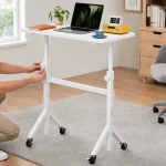 Small Standing Desk Adjustable Height with Wheels 7 | PricZone Person adjusting the height of a white wheeled adjustable desk in a bright home office with laptop plant mug and a yellow radio on the desk | PricZone