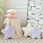 Soft pastel star cushions in white and lavender arranged around a beige fringed throw on a decorative table corner | PricZone