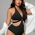 Black Plus Size Halter One Piece Swimsuit with Side Cutouts 3 | PricZone Woman in a black one piece swimsuit with cutouts gold jewelry and a white shirt draped over her arms posing against a light background | PricZone