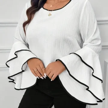 White blouse with wide, layered bell sleeves outlined in black trim, modeled with gold layered necklaces.