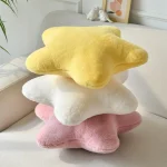 Stack of three soft star shaped plush pillows in yellow white and pink on a light colored sofa | PricZone