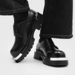 Black leather ankle boots with chunky lug soles and silver toe cap accents paired with dark denim jeans | PricZone