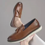 Brown leather tassel loafers with white crepe sole held against a gray background showcasing their design | PricZone