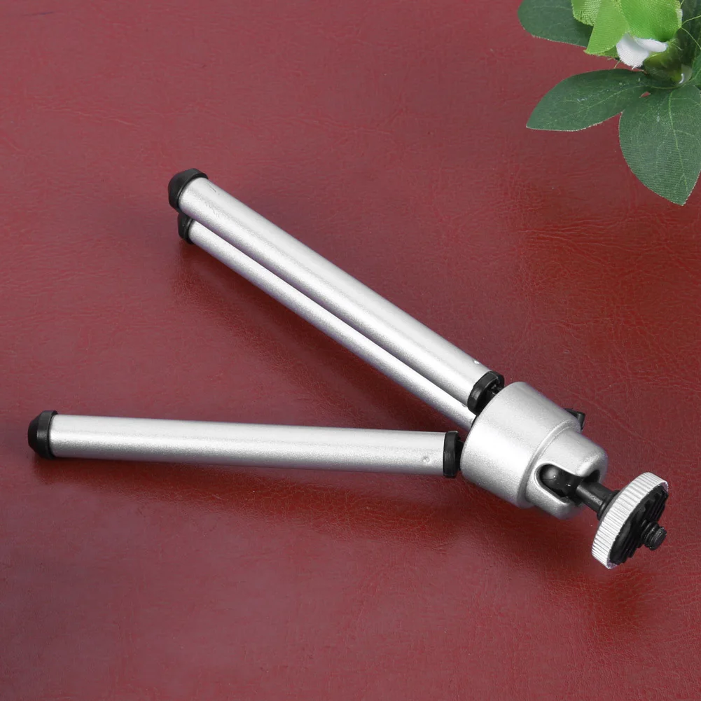 Mini tabletop camera tripod with two silver legs and a screw mount on a red surface.