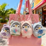 Pink tote bag with three fluffy penguin plush keychains wearing pastel hoodies each holding a lollipop outdoors on a sunny street window shopping backdrop | PricZone