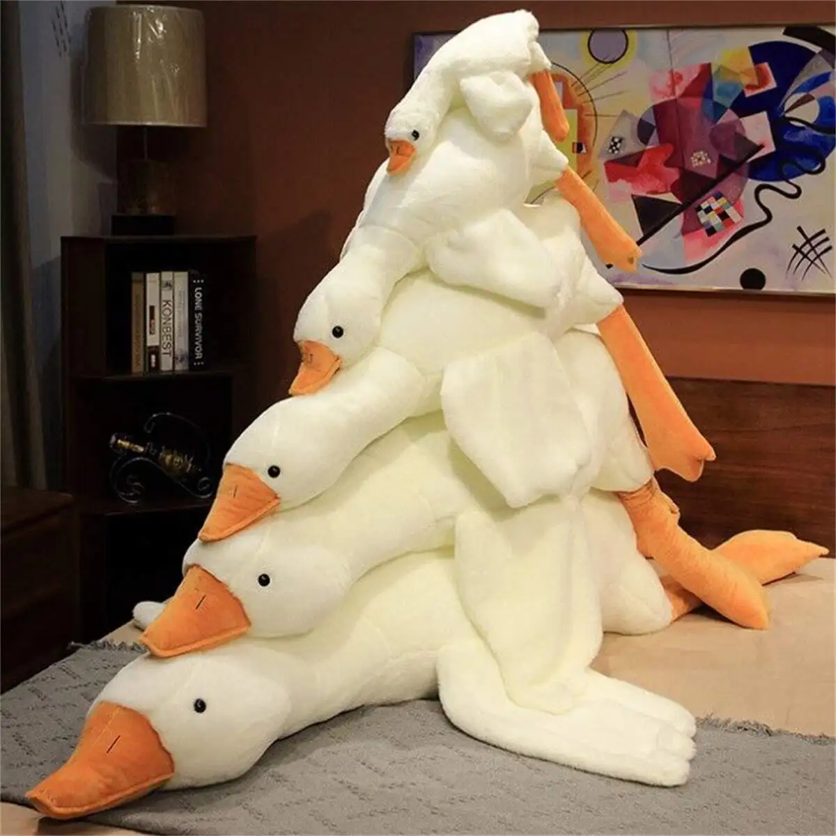 Large Plush Duck Sleep Pillow for Kids 4 | PricZone Person wearing a large white duck costume stacked with four duck shapes orange beaks in a living room with a colorful abstract painting in the background | PricZone