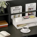 Organized desk with a black shelf two Bau Meister magazines a white twotier organizer sticky notes pencil and a coffee cup on a dark desk | PricZone