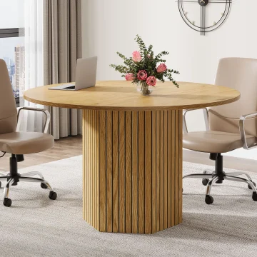 Round wooden table with a glass vase of pink flowers in a contemporary office dining area, beige swivel chairs, and a large wall clock nearby.